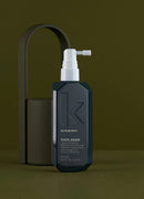 A dark charcoal gray bottle of Kevin Murphy Thick Again hair building powder with a white pump dispenser, set against a matching dark olive green background with a matching cylindrical container and arch-shaped prop.