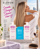 A lifestyle advertisement for ELEVEN Australia hair care products, featuring a blonde woman in a white robe in a bright bathroom setting. In the foreground, three product bottles are displayed on a marble tray: a white bottle of Anti-Frizz Shampoo, a blue 3-Minute Repair treatment bottle, and a white bottle of Anti-Frizz Conditioner - Hair Care Canada