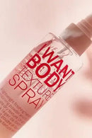 Bottle of 'I Want Body Texture Spray' on a pink background - Hair Care Canada