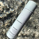A bottle of Kevin Murphy Touchable skin spray placed diagonally on rippling water, with the brand name and product name clearly visible on the bottle.