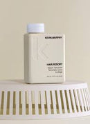 A beige rectangular hair product bottle with a white cap, labeled Kevin Murphy Hair Resort, displayed on a white slatted pedestal against a warm beige background.