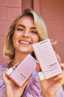 Woman holding Kevin Murphy hair products against a pink brick wall - Hair Care Canada