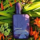 Kevin Murphy Young Again Masque hair mask in a dark purple bottle, styled among green leaves and orange flowers.